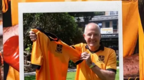 Steve Bull is holding one of the shirts in a garden and smiling at the camera. He is also wearing one.