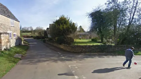 Google/LDRS A screenshot from Google street view of a junction of two country lanes. A man is walking in the middle of one of the roads and there's a cottage at the junction with a large garden.