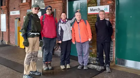 Colin Bell A group of people wearing waterproof clothing and trainers posing for a photo at March railway station