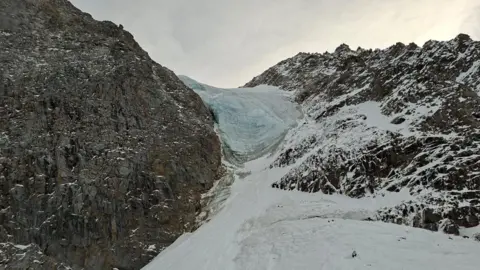 Soccorso Alpino e Speleologico A rocky mountain is seen covered in snow and a glacier 