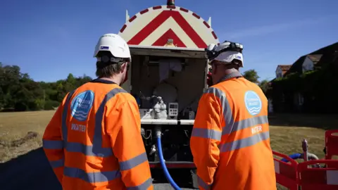 Two Thames Water workers standing behind a water tanker.