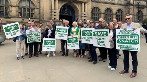 A group of people are stood outside Sheffield town hall with green and white placards