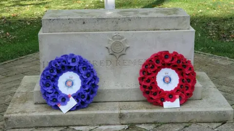 Essex Police Two wreaths of poppies, one blue and one red, sit on a stone war memorial.