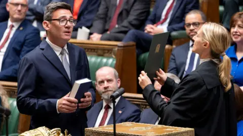 Reuters Member of Parliament (MP) for Makerfield, Andy Burnham, is sworn in at the House of Commons, in London. Labour MPs in smart dress sit on the green benches behind him