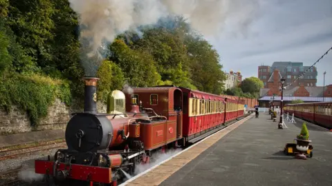 A a red stream train at Douglas Station with the platform stretching out behind it.