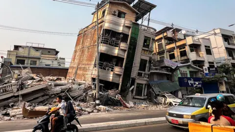 Commuters drive past a building that collapsed in the aftermath of a strong earthquake in Mandalay, Myanmar. March 30, 2025.