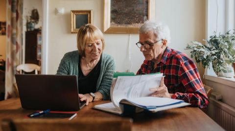 Pensioner couple look through their finances on paper and a laptop