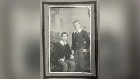 FAMILY PHOTO An old photo of Ewart and Stanley. Two boys dressed in smart black jackets with a thick white collar. The photo is black and white. 