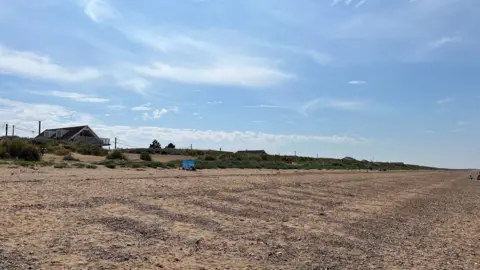 Bright blue sky above sand dunes peppered with mahram grass and a shingle beach at Heacham