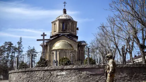 Getty Images Russian soldier walks past a church in Volnovakha during his patrol