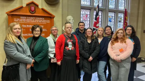 10 parents posing for a photograph looking disgruntled outside Essex County Hall's chamber in 2024.