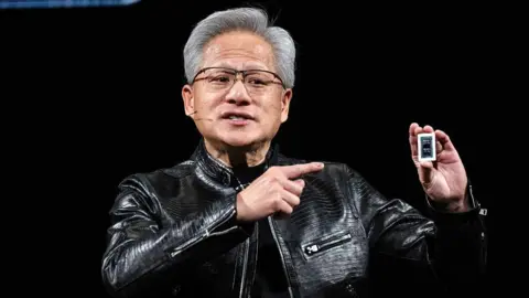 Bloomberg via Getty Images Jensen Huang is holding a computer chip in his hand and pointing at it. He is dressed in black, wearing a black leather jacket.
