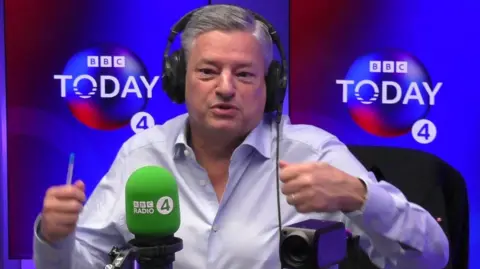BBC Ted Sarandos in the Radio 4 Today programme studio wearing headphones, in front of a microphone. He is wearing a blue shirt and has short grey-ish silver-y hair.