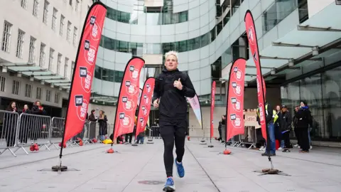 Jamie Laing running outside BBC Broadcasting House surrouned by Red Nose Day flags