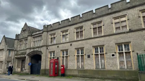 Alice Cunningham/BBC A view of the exterior of County Hall in Ipswich. The building is made of large grey bricks and has a similar look to a castle. People can be seen standing outside the building.