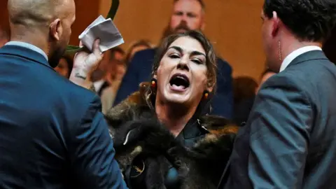 Australian Senator Lidia Thorpe is ushered out of a room by two security men as she stages a protest as Britain's King Charles and Queen Camilla attend a Parliamentary reception in Canberra, Australia on 21 October 2024