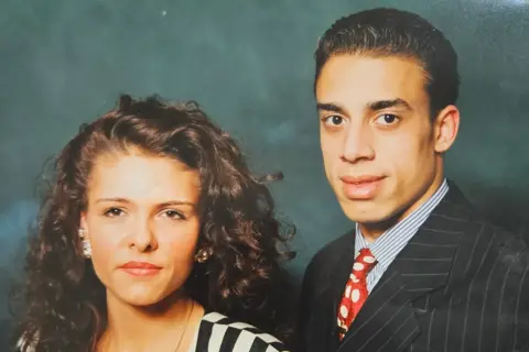 Norman Taylor A photo of a woman and a man in front of a blue background, wearing formal clothes.