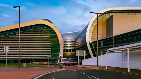The outside of Dublin Airport. It is a large curved building with steel panels and glass sides.