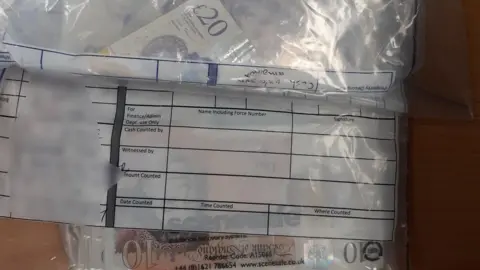 Kent Police £10 and £20 notes are seen inside a police evidence bag laid on a wooden table. 