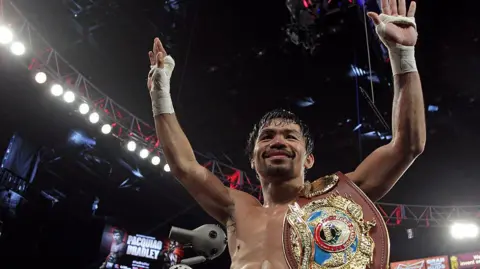 Getty Images Manny Pacquiao raises his arms after winning a fight in the boxing ring with a championship belt on his shoulder