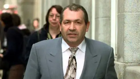 PA Media John Palmer in a grey suit, white shirt and tie walking towards the camera outside the Old Bailey in 2001.