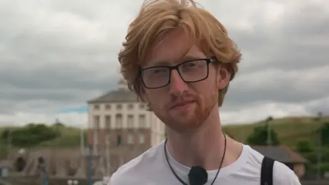 Patrick Safford at Eyemouth harbour, he has red hair, wears glasses and a white t-shirt with Berwickshire Marine Reserve on it
