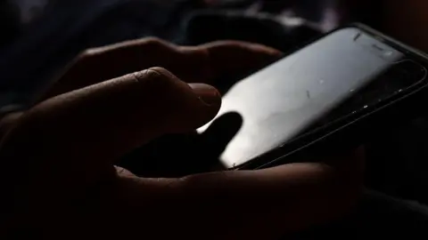 Getty Images A very close up image of someone typing on a phone. It's a dark image.