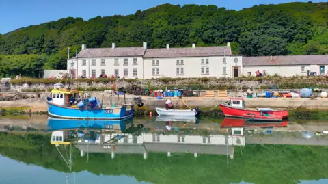 BBC Weather Watcher Jon Rathlin island harbour with blue, white and red boats tied up. There's a row of white buildings in the background. 