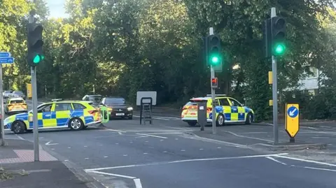 A police cordon in Hucknall Road near Nottingham City Hospital. Two police cars are blocking both sides of the road near a pedestrian crossing.