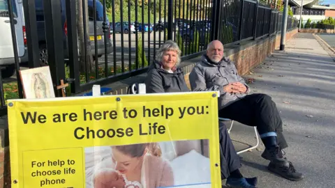 Annette and Dave sat down next to a banner which reads 'We are here to help you Choose Life'