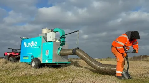 A machine which is used to clean microplastics off a beach. It looks like a giant hoover and is bright blue. 