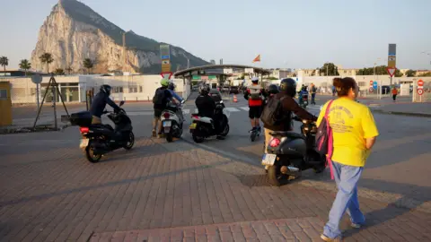 People on foot and motorbikes cross the border from Spain to Gibraltar at dawn, in front of the Rock