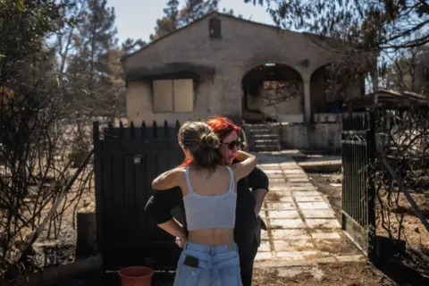 Angelos Tzortzinis / AFP Relatives comfort each other after witnessing the damage to their burnt-out home following a bushfire 