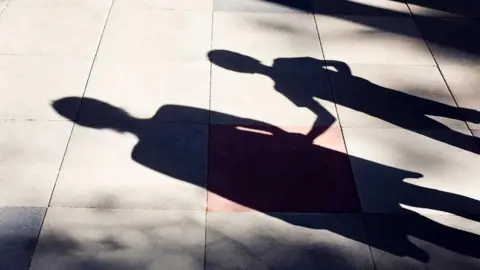 Silhouette of an adult and child on a pavement. They are holding hands.