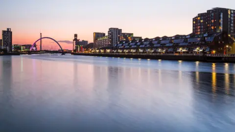 The River Clyde at night, with the sky a pink shade and buildings along the waterfront lit up with their lights on