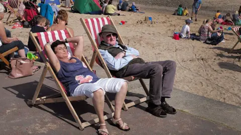 Getty Images Two people sunbathing on deckchairs