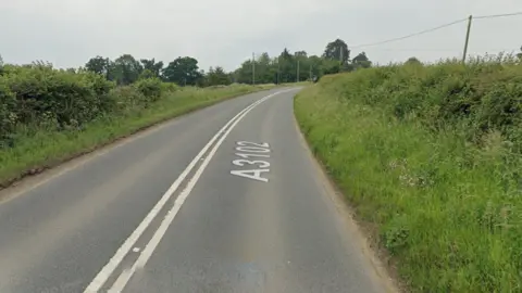 Google Maps A main road with white lines going down the middle and hedges on either side.