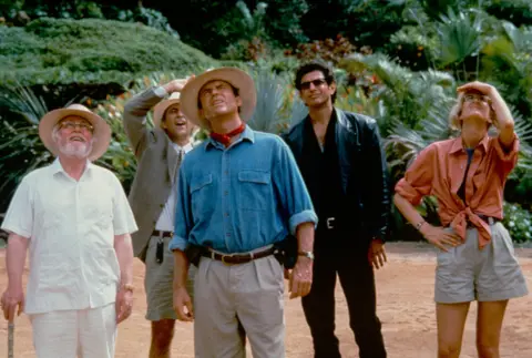 Murray Close/Moviepix/Getty Images) View of, from left, actors Richard Attenborough (in costume as John Hammond), Martin Ferrero (as Donald Gennaro), Sam Neill (as Alan Grant), Jeff Goldblum (as Ian Malcolm), and Laura Dern (as Ellie Sattler) in the film 'Jurassic Park' (directed by Steven Spielberg), 1993. (Photo by 