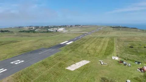 BBC Aerial view of Alderney Aiport. The runway is located between two large green spaces. 