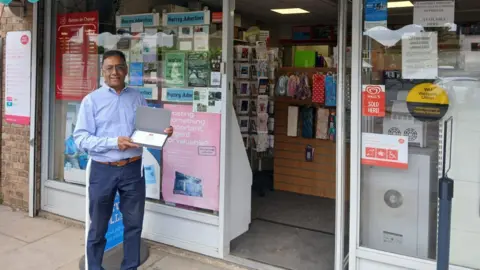 Chani Gill holding a framed certificate outside Cobham Post Office in Surrey