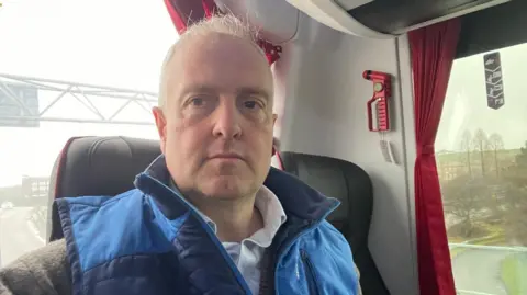 A man in a blue coat sitting on the seat of a bus