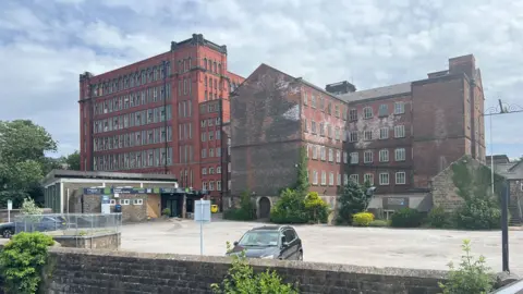 Large old victorian factory building set back infront of riverside 