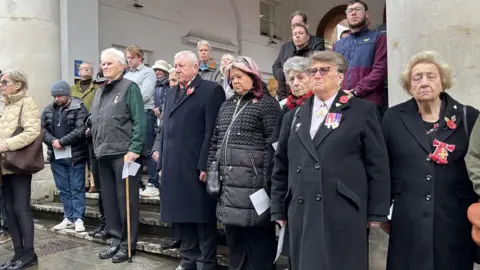 Crowds of people some with medals lower heads and mark silence in Guildford.