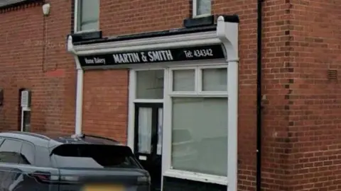 Google The front of Martin & Smith Bakery which has been painted in black and white. A black car is parked in front of the building.