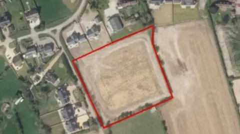 An aerial colour photo showing an area marked with a red border. There are green patches and properties elsewhere on the image.