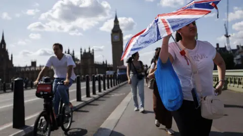 EPA/Shutterstock A woman walking away from the Big Ben holds a umbrella amid sweltering temperatures in London