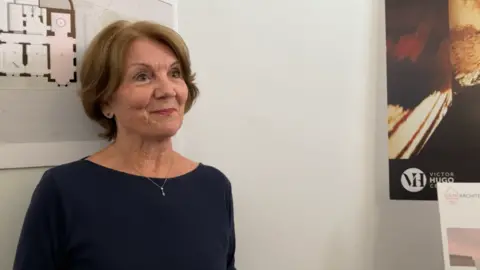 Kathryn Prince smiling and looking to the right. She has short brown hair and is wearing a blue top. 