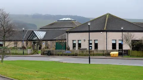 Laurencekirk Primary school building, behind a wooden fence, under a cloudy sky.