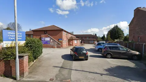 A Streetview image of Charnwood Care Home, a two storey brick building within a car park area, surrounded by residential houses