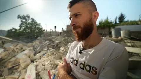 Ahmad Musa al-Qumbar stands with arms crossed in front of his destroyed home